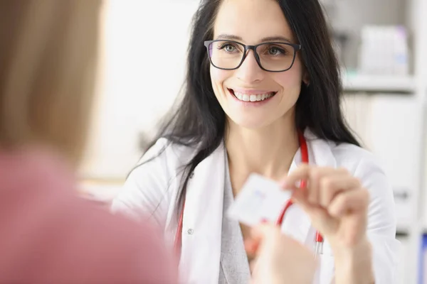 Médica sorrindo dando cartão de visita para paciente na recepção na clínica — Fotografia de Stock