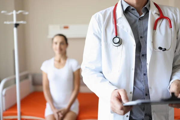 Médico com estetoscópio e documentos em suas mãos em pé na enfermaria do hospital com mulher paciente close-up — Fotografia de Stock