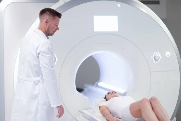 Klinikteki MRI makinesinde yatan hastanın yanında duran doktor. — Stok fotoğraf