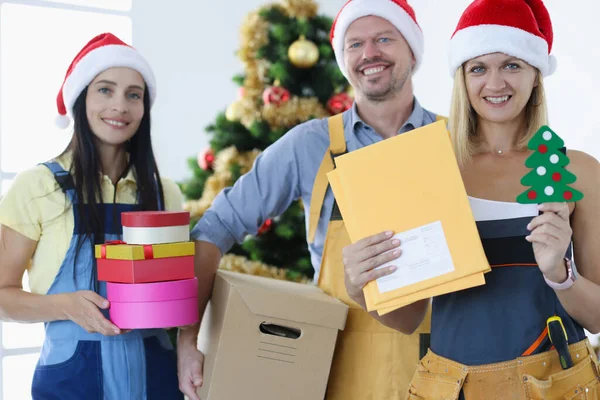 Gruppo di corrieri in cappelli Babbo Natale in piedi vicino all'albero di Natale e con in mano molte scatole regalo — Foto Stock