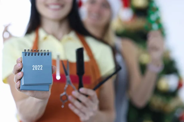 Dos mujeres sonrientes peluqueras en uniformes sostienen 2022 calendario y tijeras con un peine — Foto de Stock