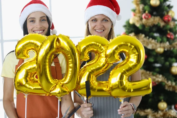 Duas mulheres sorrindo cabeleireiro em uniformes segurar números 2022 e tesoura com pente — Fotografia de Stock