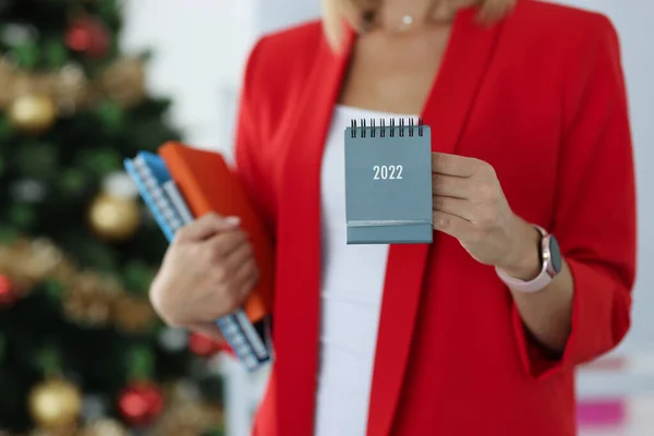Donna d'affari in giacca rossa tiene il calendario per il 2022 sullo sfondo dell'albero di Capodanno — Foto Stock