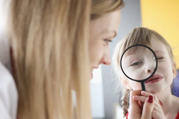 Klein meisje met vergrootglas in de buurt van haar moeder — Stockfoto