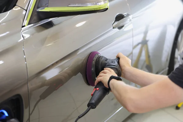 Master repairman polishing car door using special machine in workshop closeup