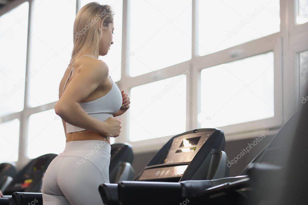 Young woman in sports uniform working out on treadmill in gym