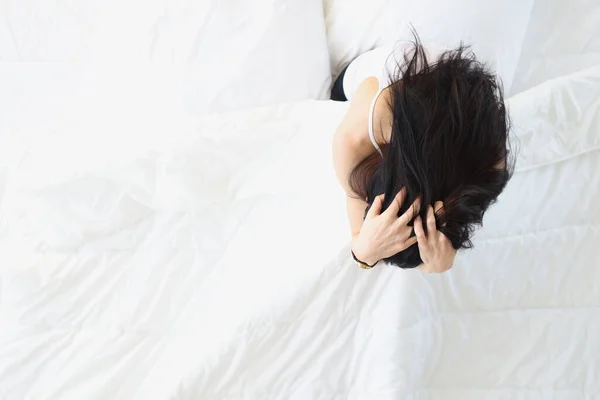 Mulher triste sentado na cama branca e segurando sua cabeça vista superior — Fotografia de Stock