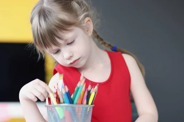 Little girl choosing multicolored pencils from glass — Stock Photo, Image