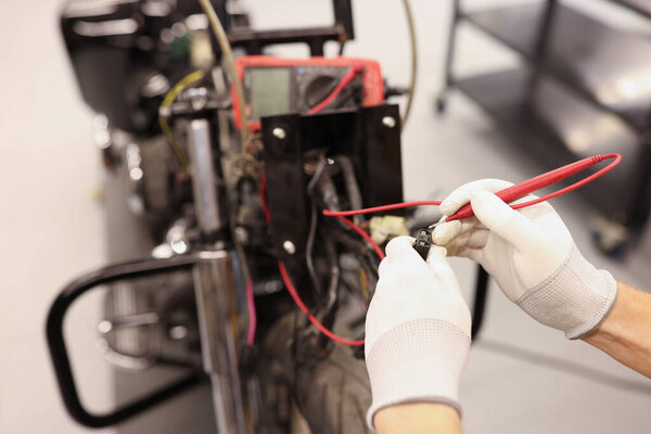 Male repairman checking electrics of motorcycle using tester closeup