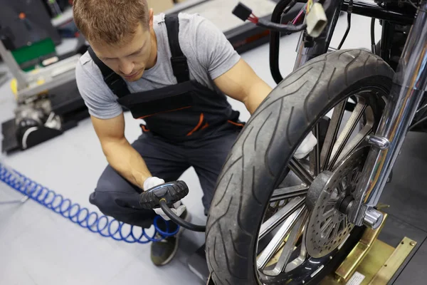 Man repairman inflating motorcycle tires in auto repair shop