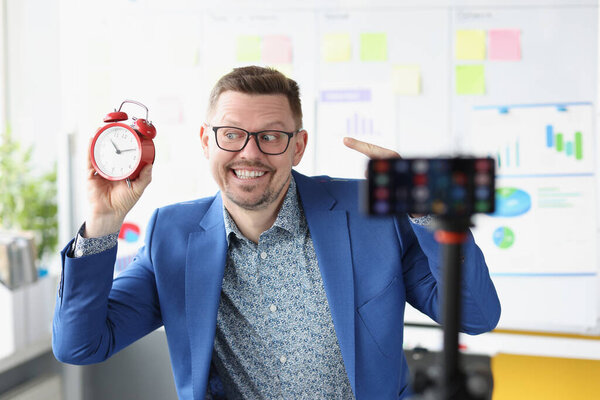 Young male blogger shoots video witha red alarm clock on camera