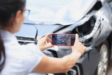 Sigortacı kadın, araba kazasından sonra akıllı telefondan araba hasarının fotoğraflarını çekiyor.