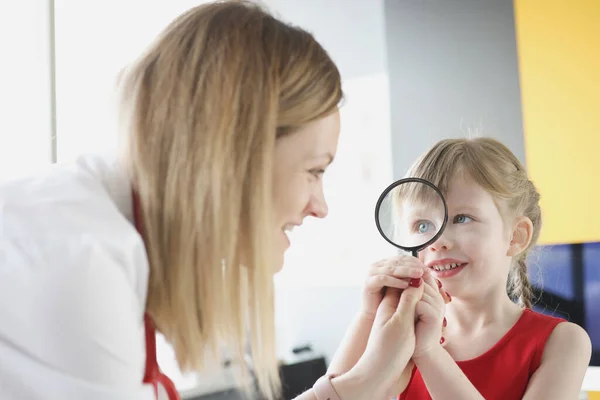 Pediatrician doctor with little girl holding magnifying glass. — Stock Photo, Image