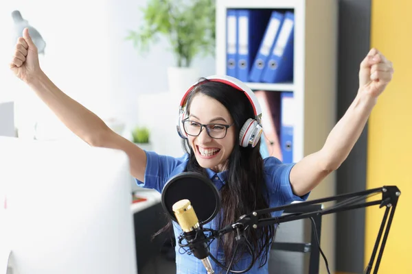 Радостная улыбающаяся женщина с энтузиазмом поднимает руки в наушниках и микрофонах и смотрит на монитор компьютера — стоковое фото