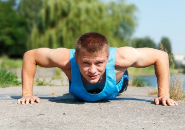 Handsome young man in good shape doing push-up while outdoor tra clipart