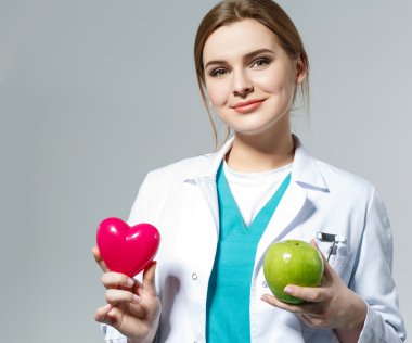 Beautiful smiling female doctor holding red heart and green appl