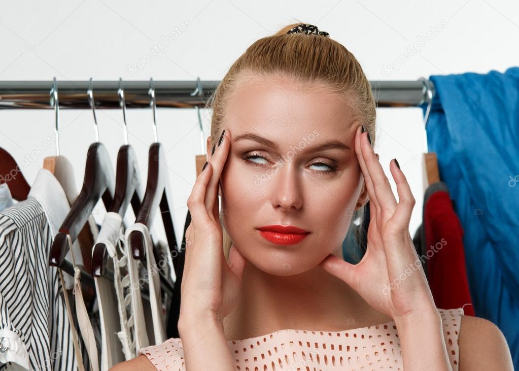 Beautiful blonde woman suffering near wardrobe rack