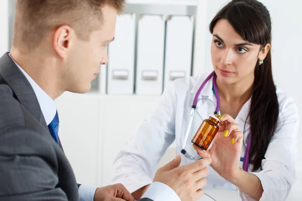 Beautiful female medicine doctor giving pills to male patient — Stockfoto