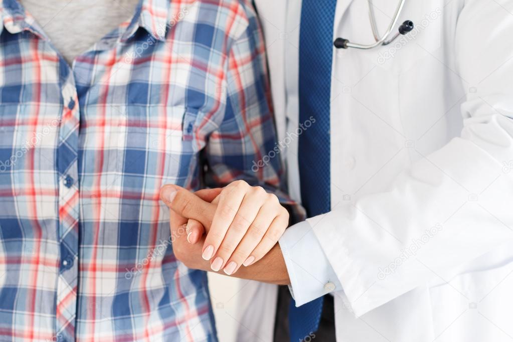Friendly male doctor hands holding female patient hand
