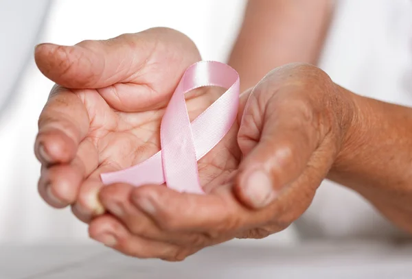 Donna anziana mani che tengono il nastro rosa consapevolezza del cancro al seno — Foto Stock