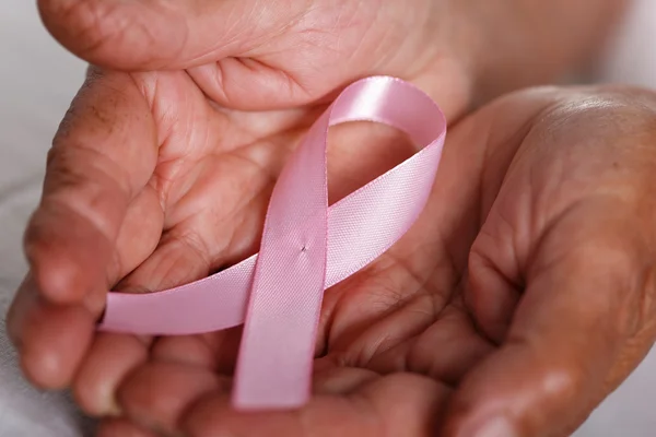 Donna anziana mani che tengono il nastro rosa consapevolezza del cancro al seno — Foto Stock