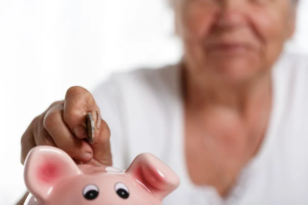 Anciana poniendo monedas de dinero pin en la ranura rosa de Piggybank —  Fotos de Stock