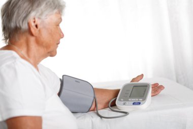 Elder woman measuring blood pressure with automatic manometer at
