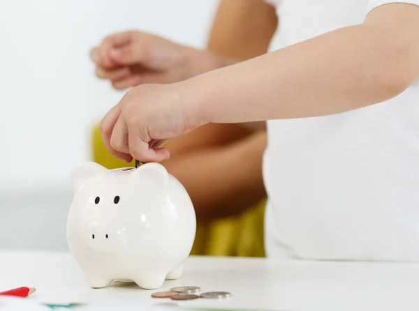 Mano de niño poniendo monedas de dinero pin en la ranura blanca de Piggybank —  Fotos de Stock