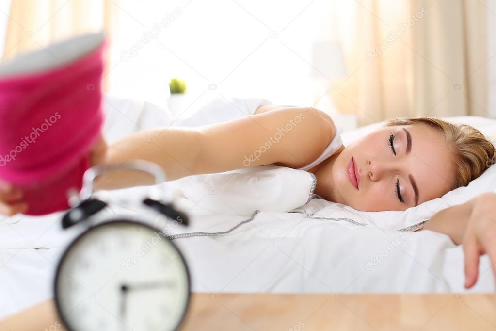 Sleepy young beautiful woman trying kill alarm clock
