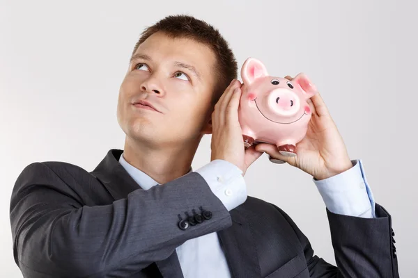 Businessman in suit and tie shaking funny piggybank Stock Photo