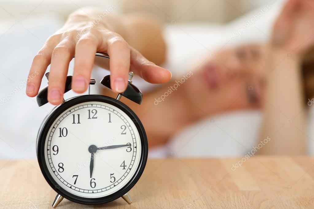 Stretching hand of sleepy young woman trying kill alarm clock