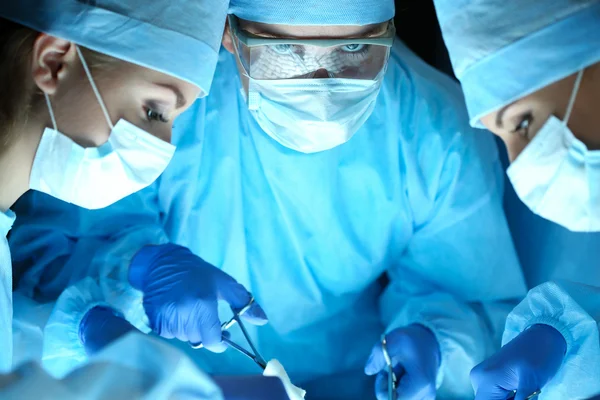 Three surgeons at work operating in surgical theatre — Stock Photo, Image