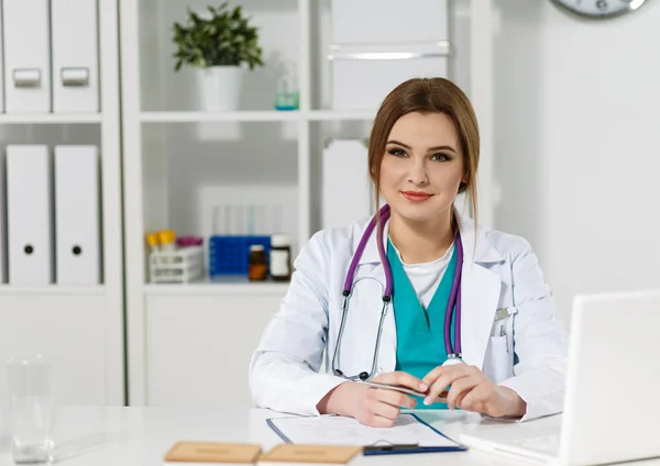 Mooie vriendelijke vrouwelijke arts zit op werktafel — Stockfoto