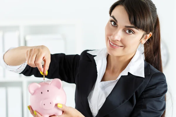 Mulher bonita feliz colocando moedas de dinheiro pin em rosa piggyban — Fotografia de Stock