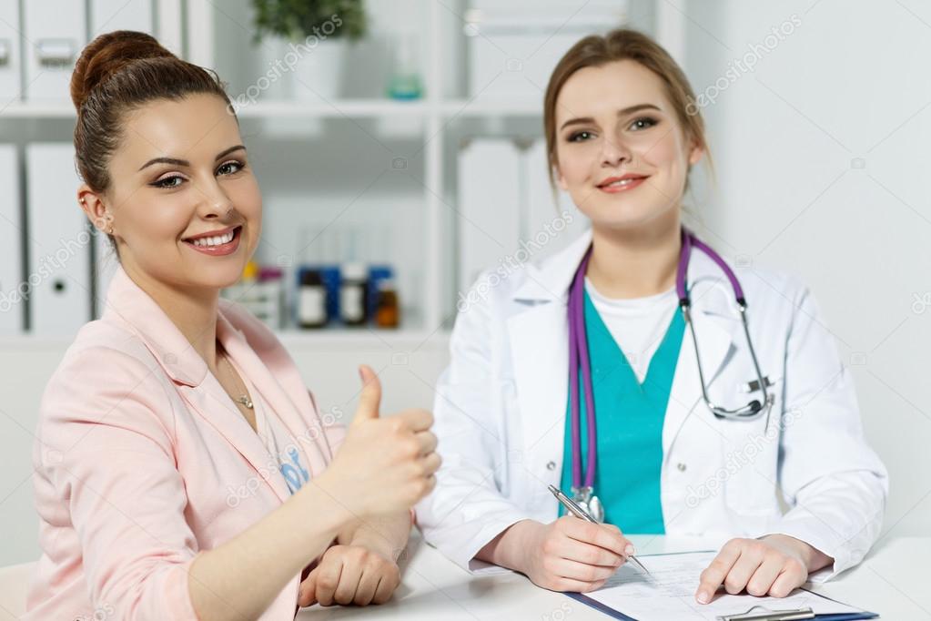 Smiling woman showing OK sign with thumb up at physician recepti