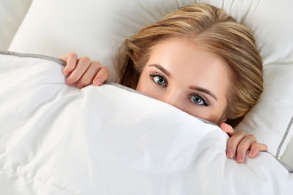 Güzel sarışın kadın yatakta örtü altında yatan yüzünü gizleme