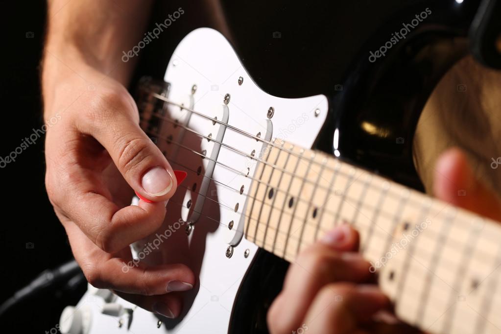 Male hands playing electric guitar with plectrum closeup