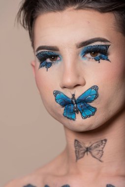 Bej arka planda mavi kelebek makyajlı genç model adam ve kopyalama alanı.