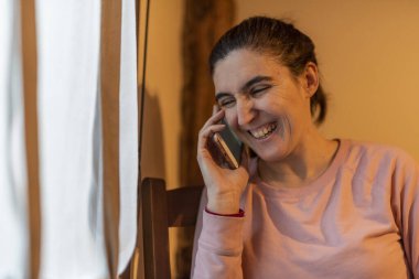 Pencere kenarında telefonla konuşan gülen kadın.