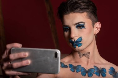 Yaratıcı makyajlı genç adam cep telefonuyla selfie çekiyor.