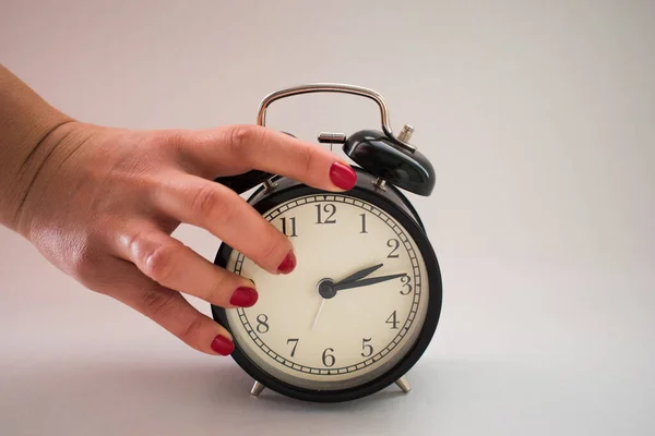 Woman with red colored nails holding alarm clock as reaction to stop its alarm sound. Wake up call. Close up shot.