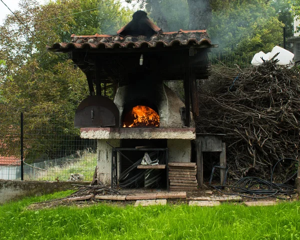 External wood oven with green grass terrain in the foreground. Traditional pizza oven burning wood. Flame in the furnace.