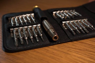 Ahşap bir arka planda izole edilmiş siyah deri bir çantadaki alet çeliğinden yapılmış tornavida parçaları.