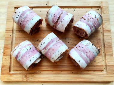 Et, ahşap bir masada domuz pastırmasında yuvarlanıyor. Yemek pişirme süreci.