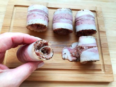 Et, ahşap bir masada domuz pastırmasında yuvarlanıyor. Yemek pişirme süreci.