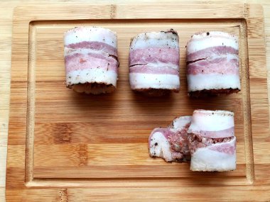 Et, ahşap bir masada domuz pastırmasında yuvarlanıyor. Yemek pişirme süreci.