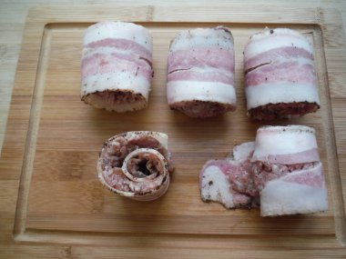 Et, ahşap bir masada domuz pastırmasında yuvarlanıyor. Yemek pişirme süreci.