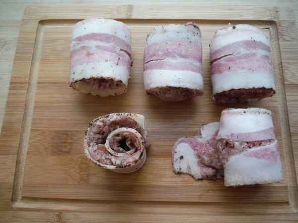 Et, ahşap bir masada domuz pastırmasında yuvarlanıyor. Yemek pişirme süreci.