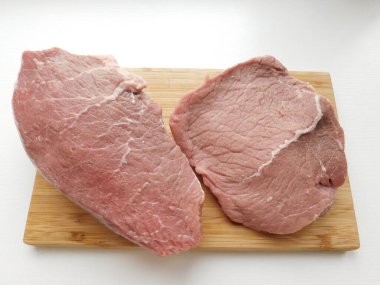 Ahşap bir masanın üzerindeki tahta kesme tahtasının üzerinde iki domuz bifteği. Et yemekleri için malzemeler