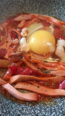 Lezzetli, sulu, geleneksel Akdeniz yemeği Shakshuka. Tahta kesme tahtasının üstünde, siyah bir tavada. Domates ve sahanda yumurta, baharatlar. Üst görünüm kapat.